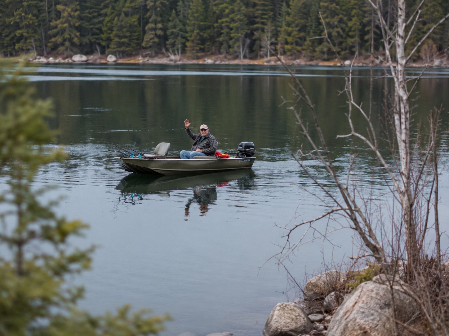 A lone boater offers a half-wave across a calm Misquah lake.