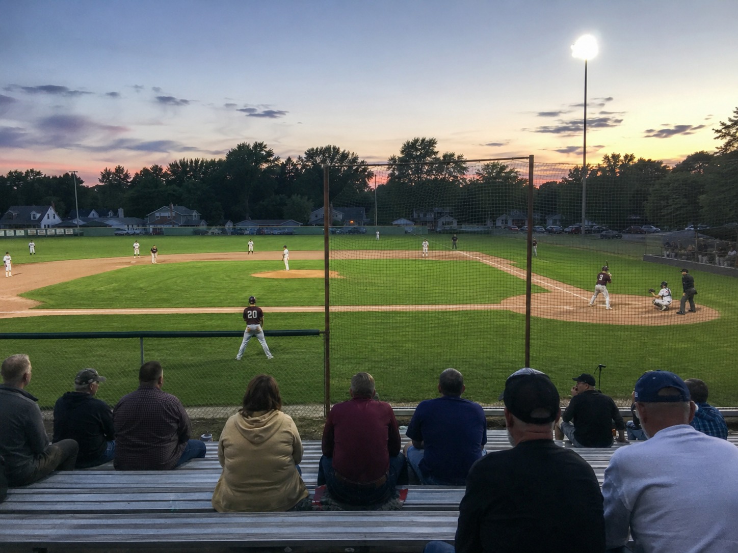 Fans settle into the bleachers for a Legion baseball game at dusk.